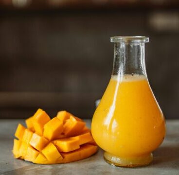 A refreshing and vibrant mango juice served in a clear glass bottle next to ripe mangos.